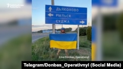 Украинский военный с флагом Украины у указателя с направлениями на населенные пункты в Курской области РФ. Август 2024 года