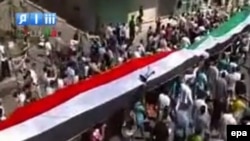 Protesters hold a giant current Syrian national flag (red, white, black) and a former national flag (green, white, black) during a protest allegedly in Palmyra, in the Homs district, on September 2. 