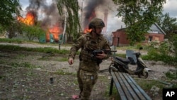 Полицейский бежит впереди горящего дома, разрушенного российским авиаударом в Волчанске, 11 мая 2024 года